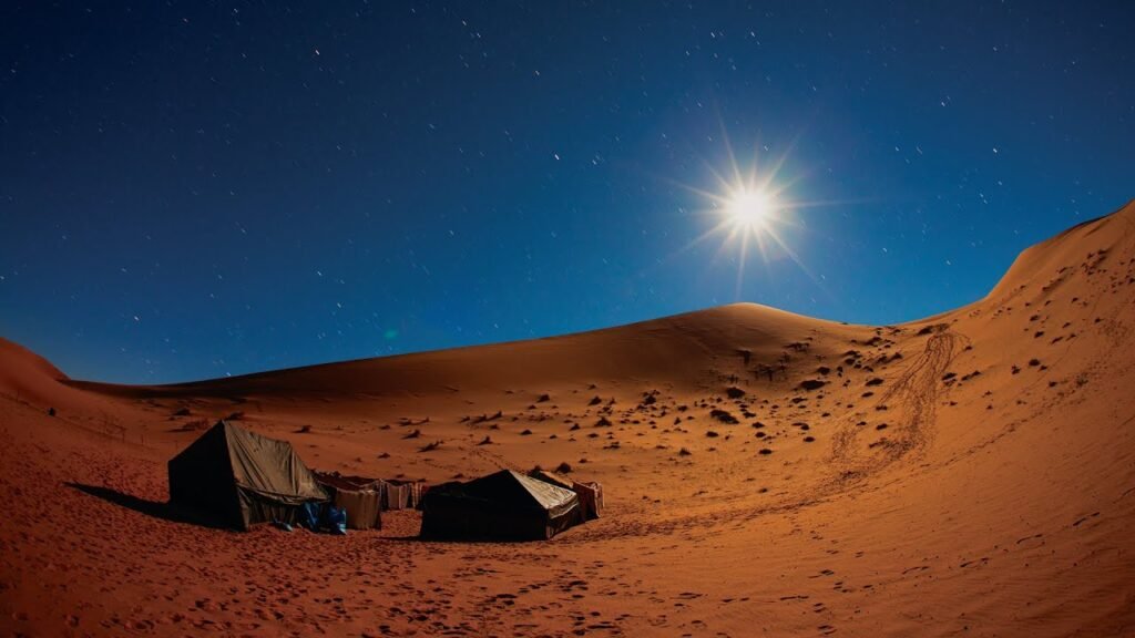 A clear night sky full of stars above the golden sand dunes in the Dubai desert, with a group of people enjoying a stargazing experience.